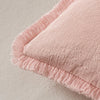 A soft, dusty pink throw pillow cover with a fringe edge and natural linen texture.