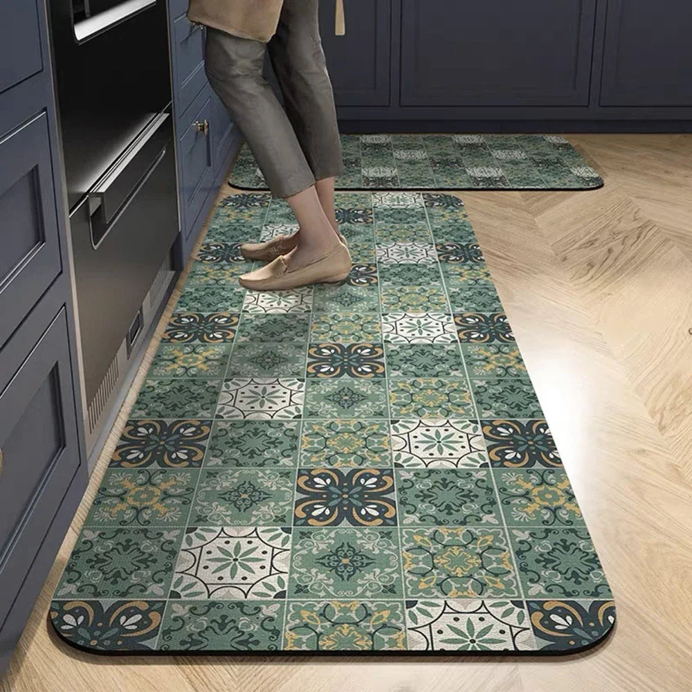 A rectangular green and beige patterned non-slip absorbent floor mat placed on a light wood floor.