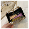 A hand holds an open gold envelope clutch with a chain strap, revealing makeup products inside.