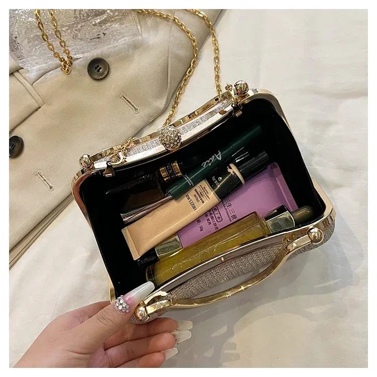 A hand holds an open gold envelope clutch with a chain strap, revealing makeup products inside.