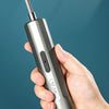 A hand holds a silver cordless electric screwdriver with a sharp tip and a button, against a dark blue background.