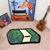 A green and black mat with a white dollar bill design is placed on a light wood floor.