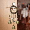 A rustic witch bells door hanger wind chime made of dark wood and brass hanging on a light-colored wall.