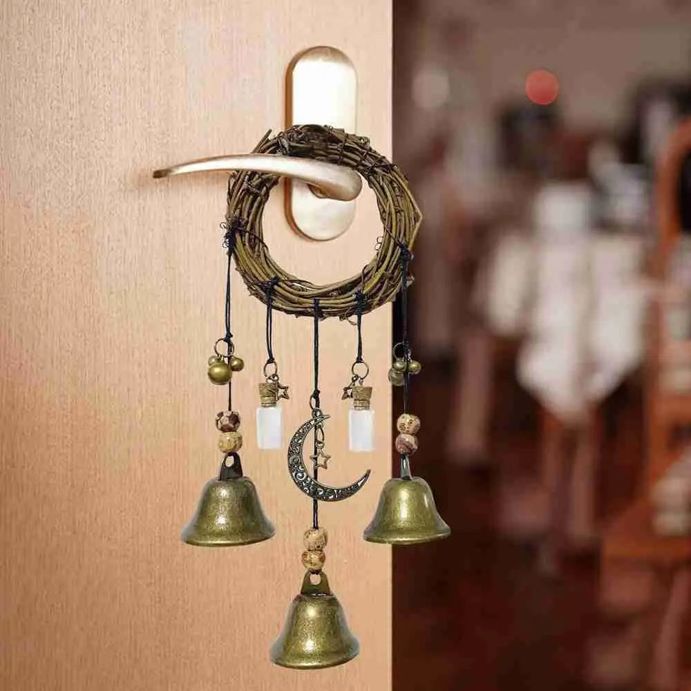A rustic witch bells door hanger wind chime made of dark wood and brass hanging on a light-colored wall.