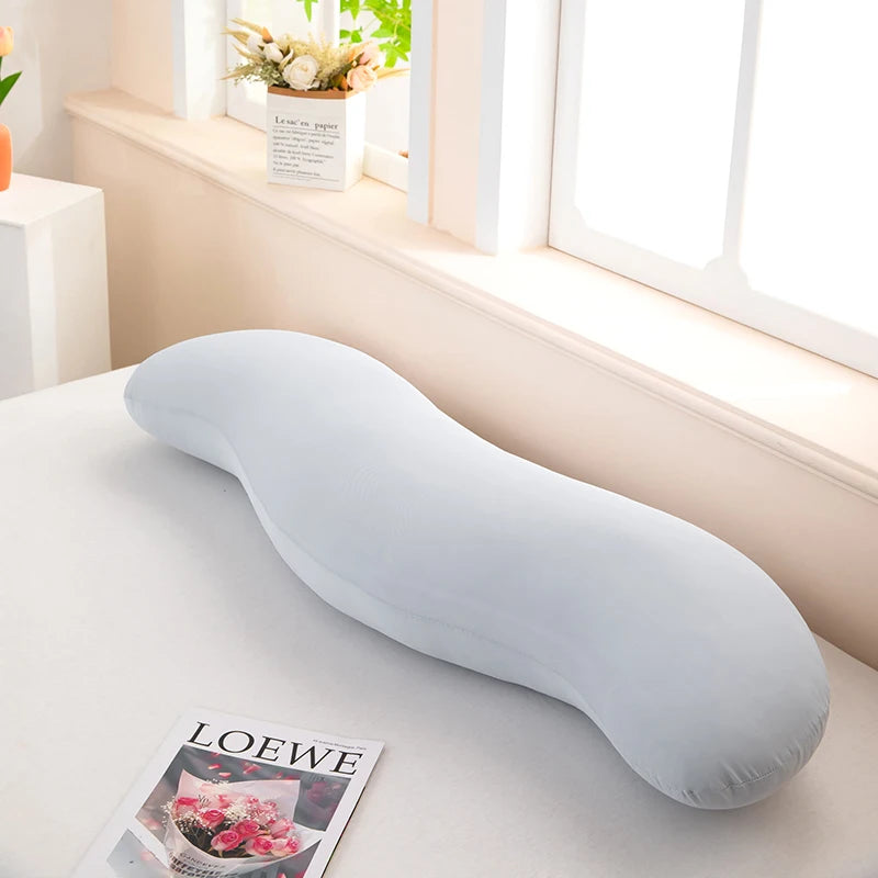 Almohada lateral de onda ergonómica gris claro, acostada sobre una superficie blanca junto a una ventana.