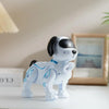 A white interactive robot dog with black ears and blue accents sits on a white surface.