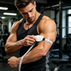 A muscular man is using an automatic retractable body measuring tape on his arm in a gym setting.