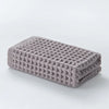 A stack of gray waffle weave bath towels folded neatly on a white surface.