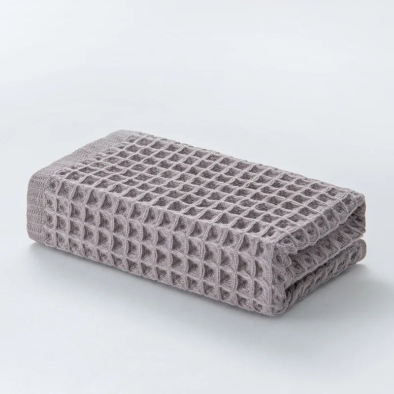 A stack of gray waffle weave bath towels folded neatly on a white surface.