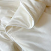 A white lightweight ice silk quilt or blanket is folded and draped on a soft fabric background.