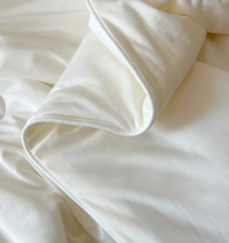 A white lightweight ice silk quilt or blanket is folded and draped on a soft fabric background.