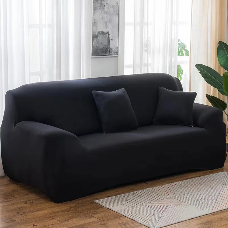 A modern black elastic stretch sofa cover for a 3-seater sofa placed in a bright living room.