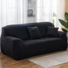 A modern black elastic stretch sofa cover for a 3-seater sofa placed in a bright living room.