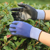 A hand wearing a dark leather work glove and a blue PU-coated work glove resting on green foliage.