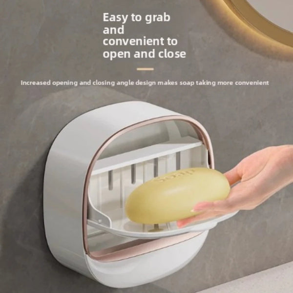 A hand is opening a wall-mounted soap holder with a lid and drainage feature.