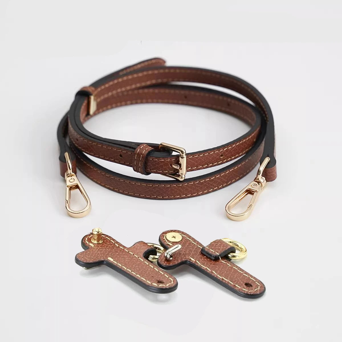 Brown leather shoulder strap with brass hardware coiled on a white background.