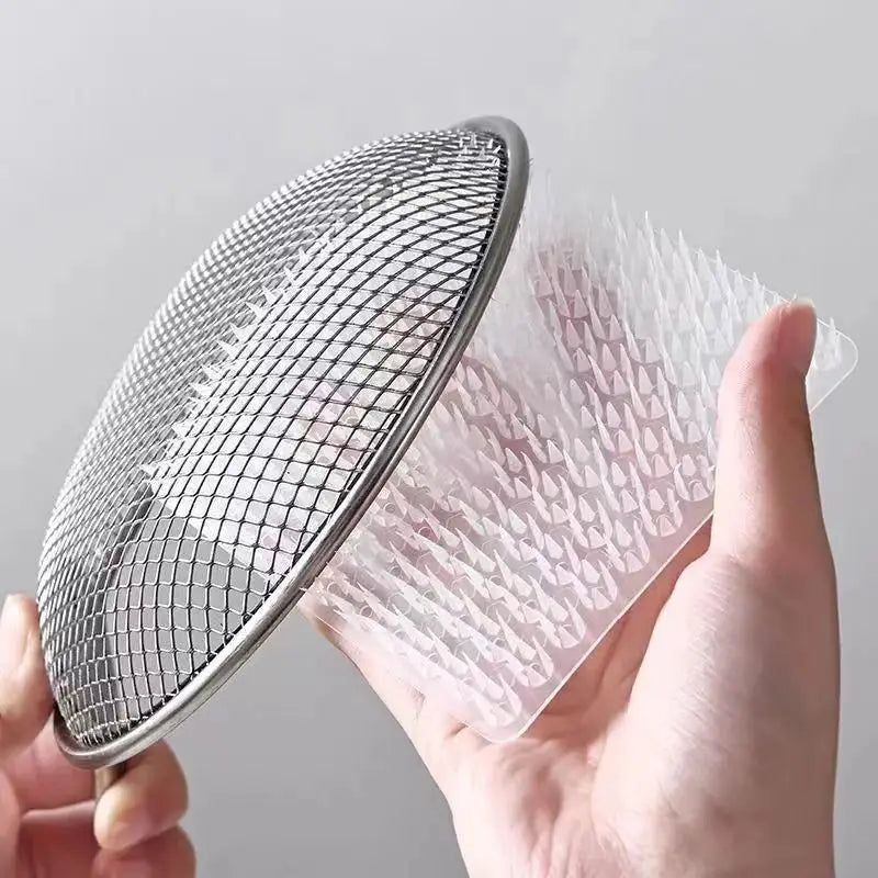 Une main tient un set de tamis silicone et brosse à fissures argentés contre une surface plastique translucide.