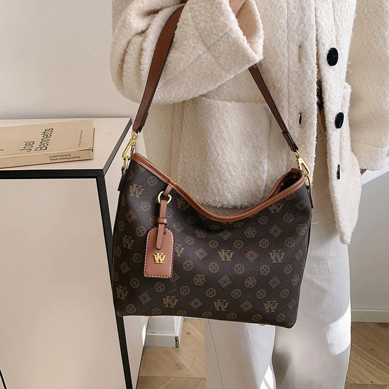A brown leather tote bag with a gold strap and a patterned fabric is shown against a white coat.