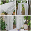Two sheer white floral lace curtains hanging outdoors in a garden setting.