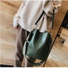 A woman wearing a beige sweater holds a dark green alligator pattern crossbody bag.
