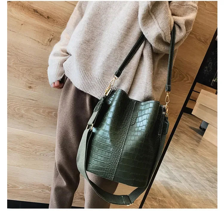 A woman wearing a beige sweater holds a dark green alligator pattern crossbody bag.