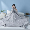 A gray cooling summer quilt is draped on a bed, with a person resting their head on the fabric.