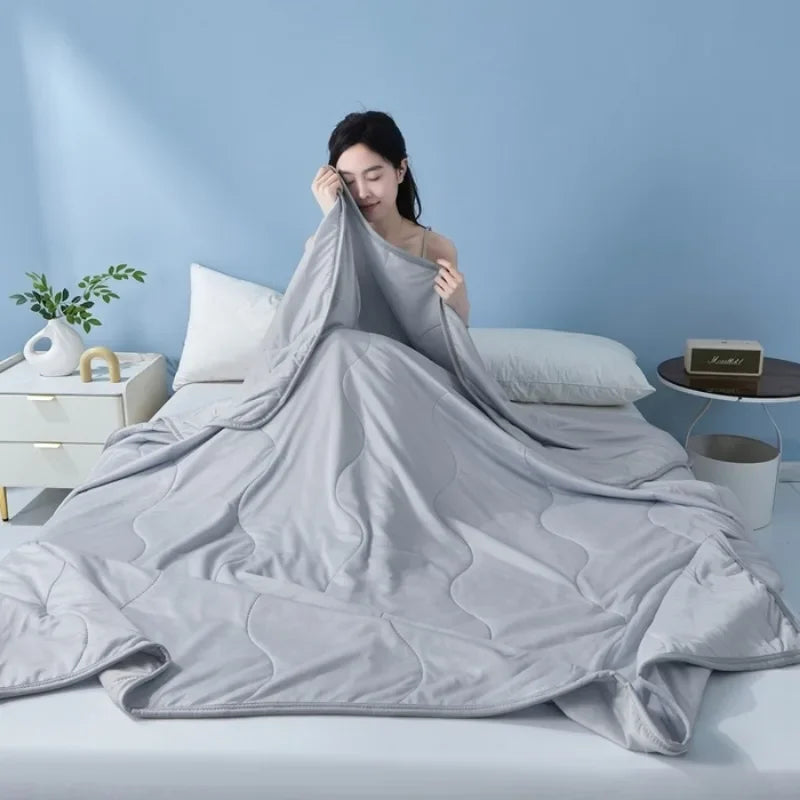 A gray cooling summer quilt is draped on a bed, with a person resting their head on the fabric.