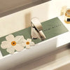 A silver faucet mat with a floral design rests on a light green cutting board next to a glass jar.