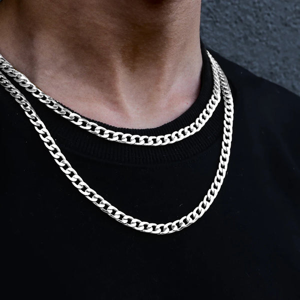 Primer plano de un collar de eslabones cubanos plateado usado alrededor del cuello contra una camisa negra.