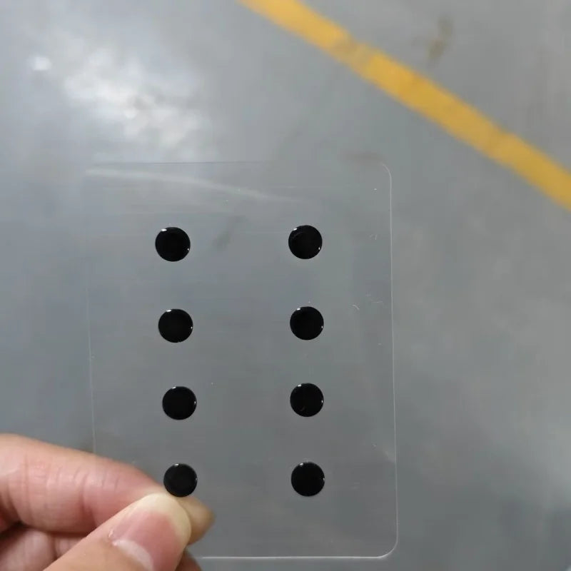 A hand is placing smooth glass mouse skates onto a clear plastic sheet for use with gaming or office mice.