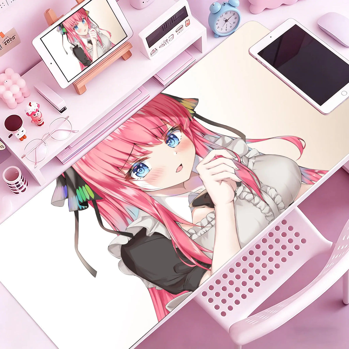 A drawing of an anime girl with pink hair relaxing on a pink desk mat next to various stationery items and a tablet.