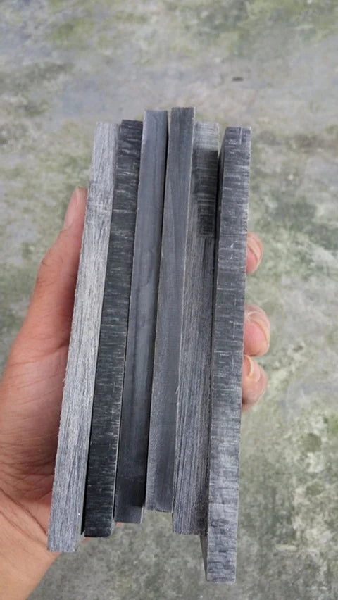 A hand holds a stack of black buffalo horn knife handle scales.