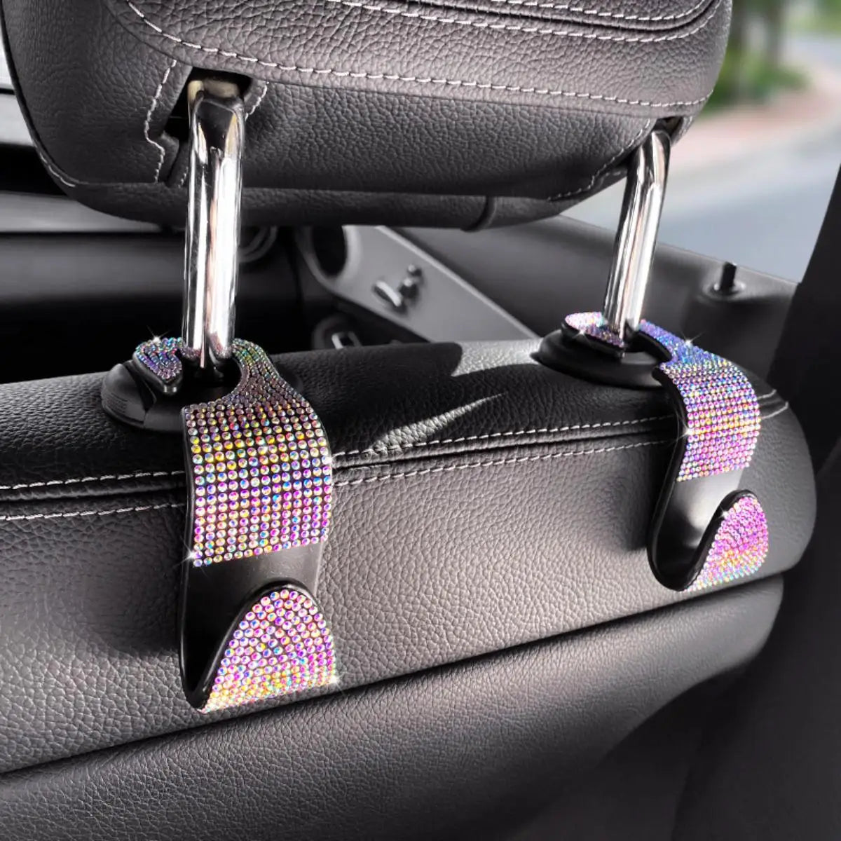 A close-up of a car seat storage hook set featuring crystal diamond accents on black leather upholstery.