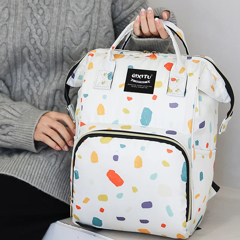 A white and colorful patterned waterproof backpack diaper bag with black trim being held by a person.