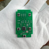 A green electronic circuit board is held in a person's hand.