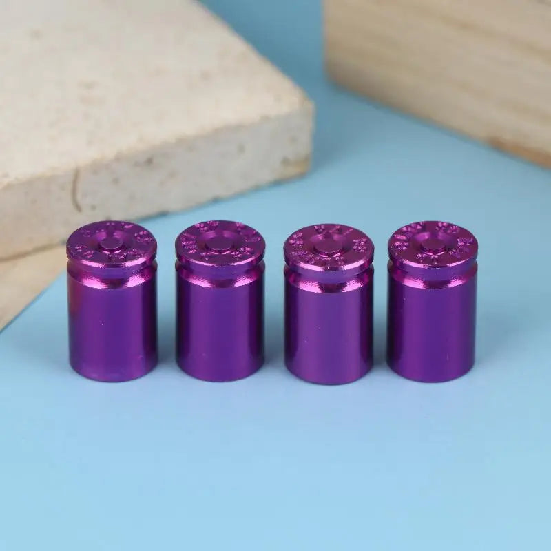A set of four metallic purple bullet shell tire valve stem caps resting on a light blue surface.