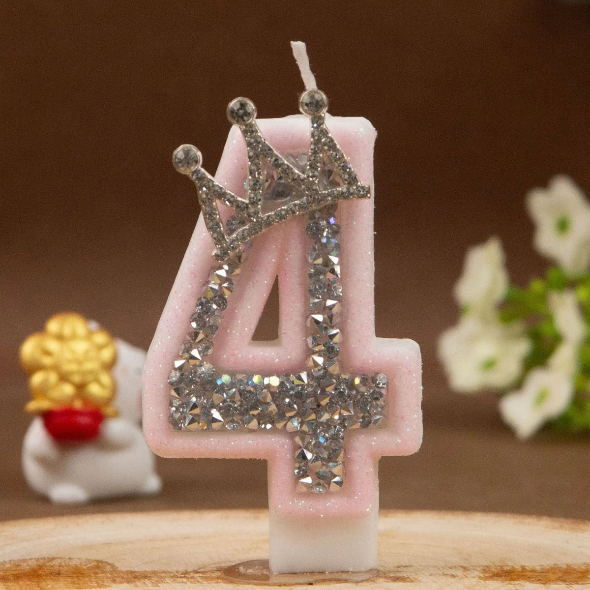 A pink rhinestone crown number candle shaped like the number 4 sits on a wooden surface.