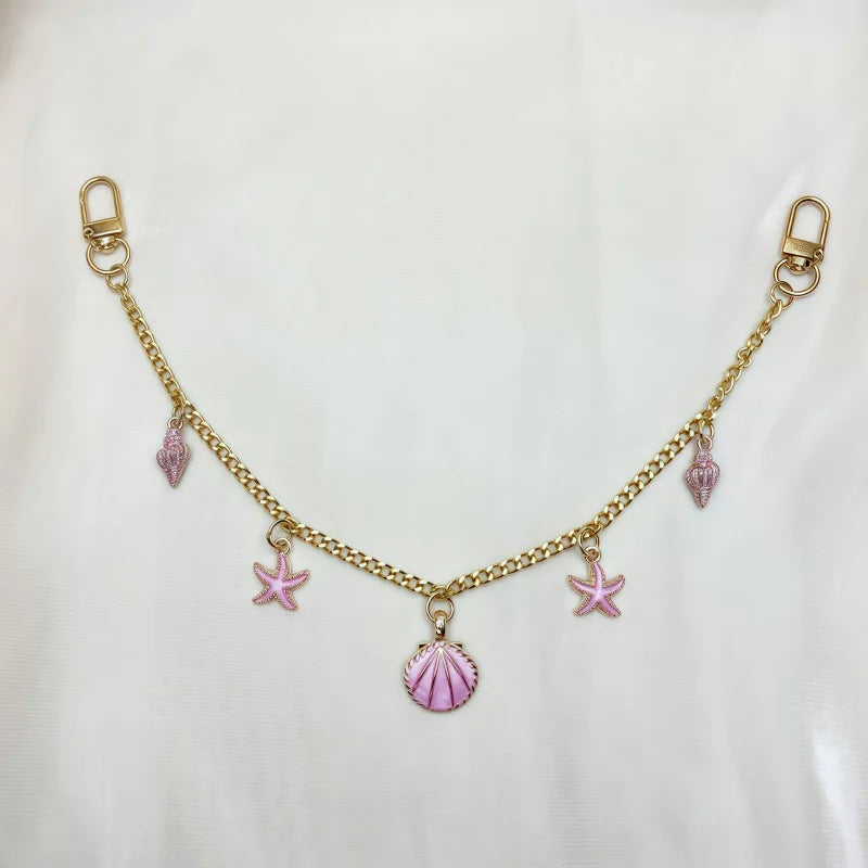 Gold alloy chain with pink starfish and seashell charms on a white background