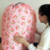 A pink drawstring laundry bag with a cherry pattern is being held by a woman.