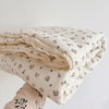 A stack of floral muslin baby blankets in cream and beige tones, folded and stacked on a white surface.