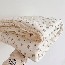 A stack of floral muslin baby blankets in cream and beige tones, folded and stacked on a white surface.