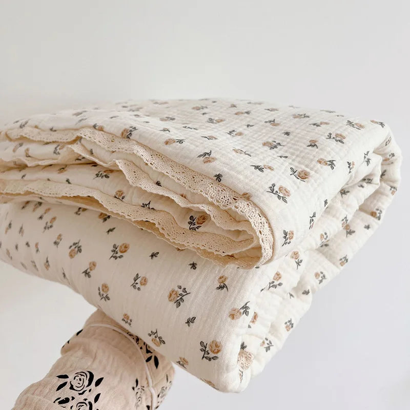 A stack of floral muslin baby blankets in cream and beige tones, folded and stacked on a white surface.