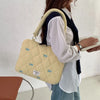 A woman is holding a light yellow quilted laptop shoulder bag with a navy strap and padding.