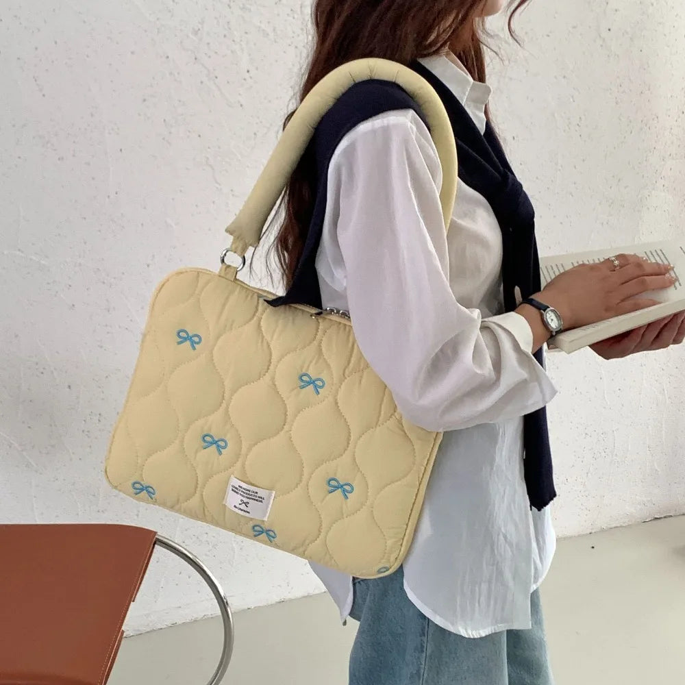 A woman is holding a light yellow quilted laptop shoulder bag with a navy strap and padding.