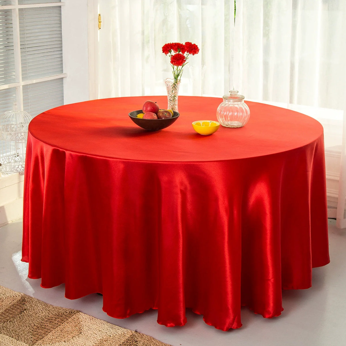 A round red satin tablecloth set for an event featuring fruit and a glass vase.
