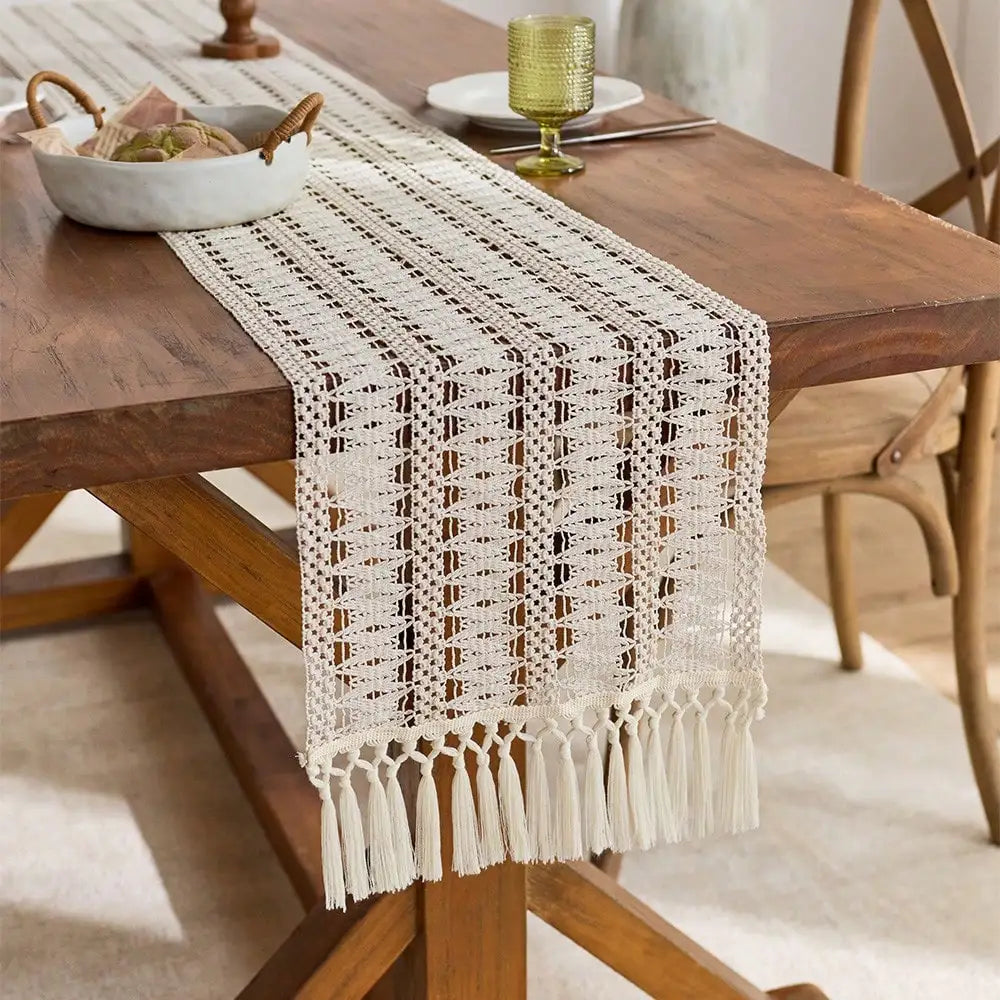 A beige macrame table runner with fringe is displayed on a wooden dining table.