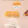 A hand is using a yellow electrostatic duster with orange fuzzy refills to clean dust from a surface.