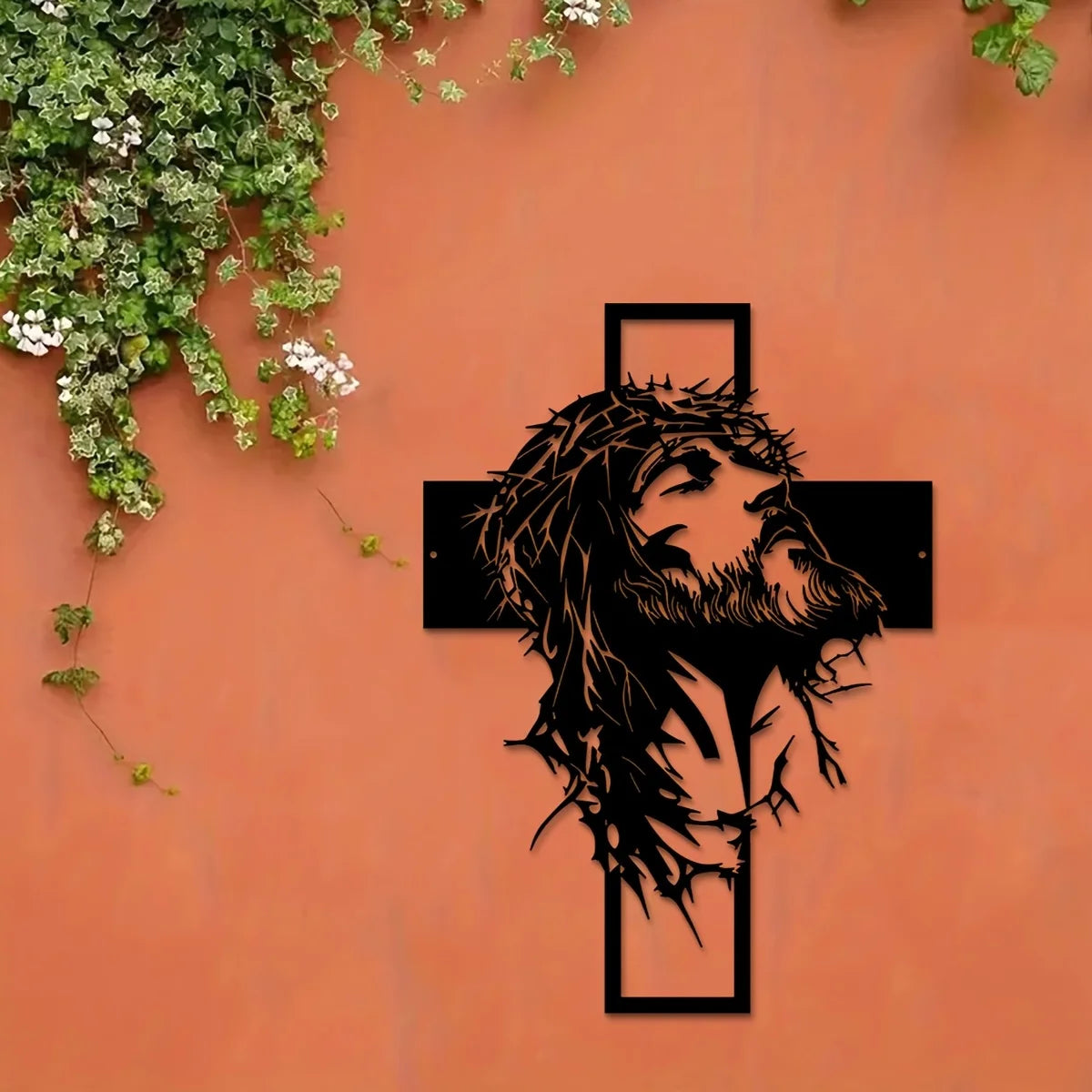 Silhouette de la tête et de la barbe de Jésus en métal noir avec une croix sculptée dans un mur de terre cuite recouvert de l