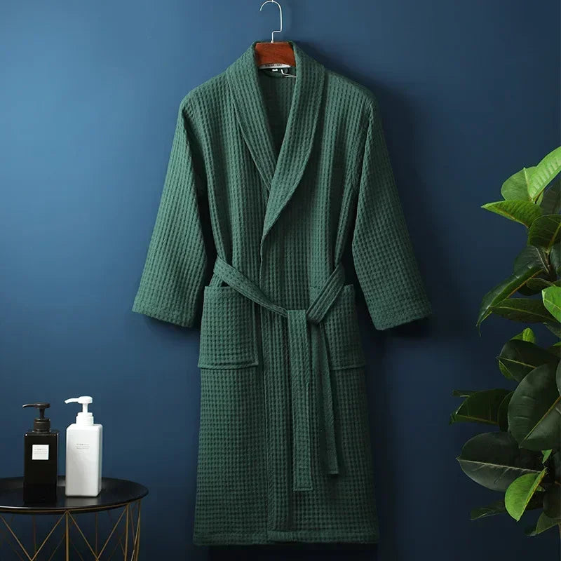 A dark green lightweight cotton waffle robe hanging on a wall against a blue background.