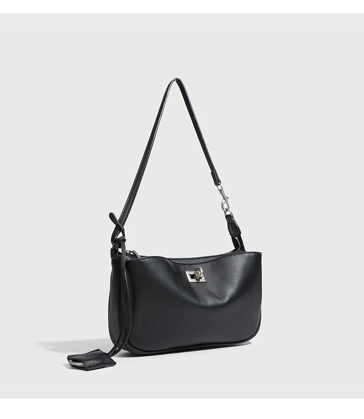 A black leather tote bag with a long strap and a metal buckle displayed against a light gray background.